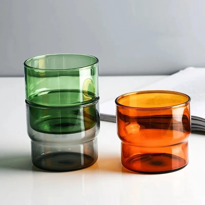 Copo de Vidro No. 05 Pure Mineral em borossilicato empilhável verde e âmbar pousado sobre superfície de areia com luz natural.